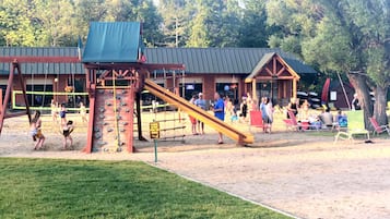 Une aire de jeux avec un toboggan et un mur d’escalade, entourée d’un bâtiment avec un toit rouge et d’un panneau indiquant : « Veuillez ne pas nourrir les canards. »