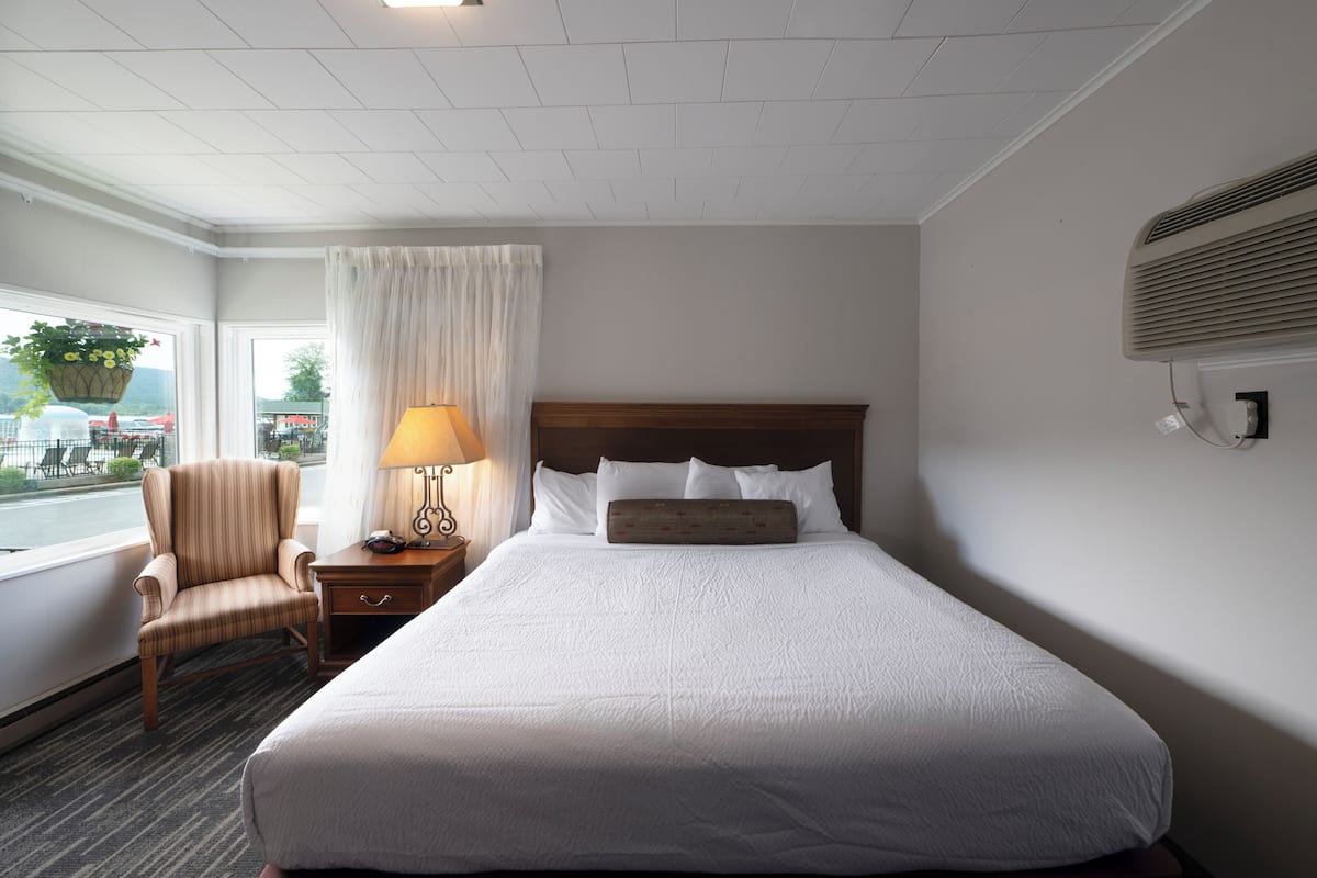 A hotel room with a large bed, a chair, a nightstand with a lamp, and a window with curtains.