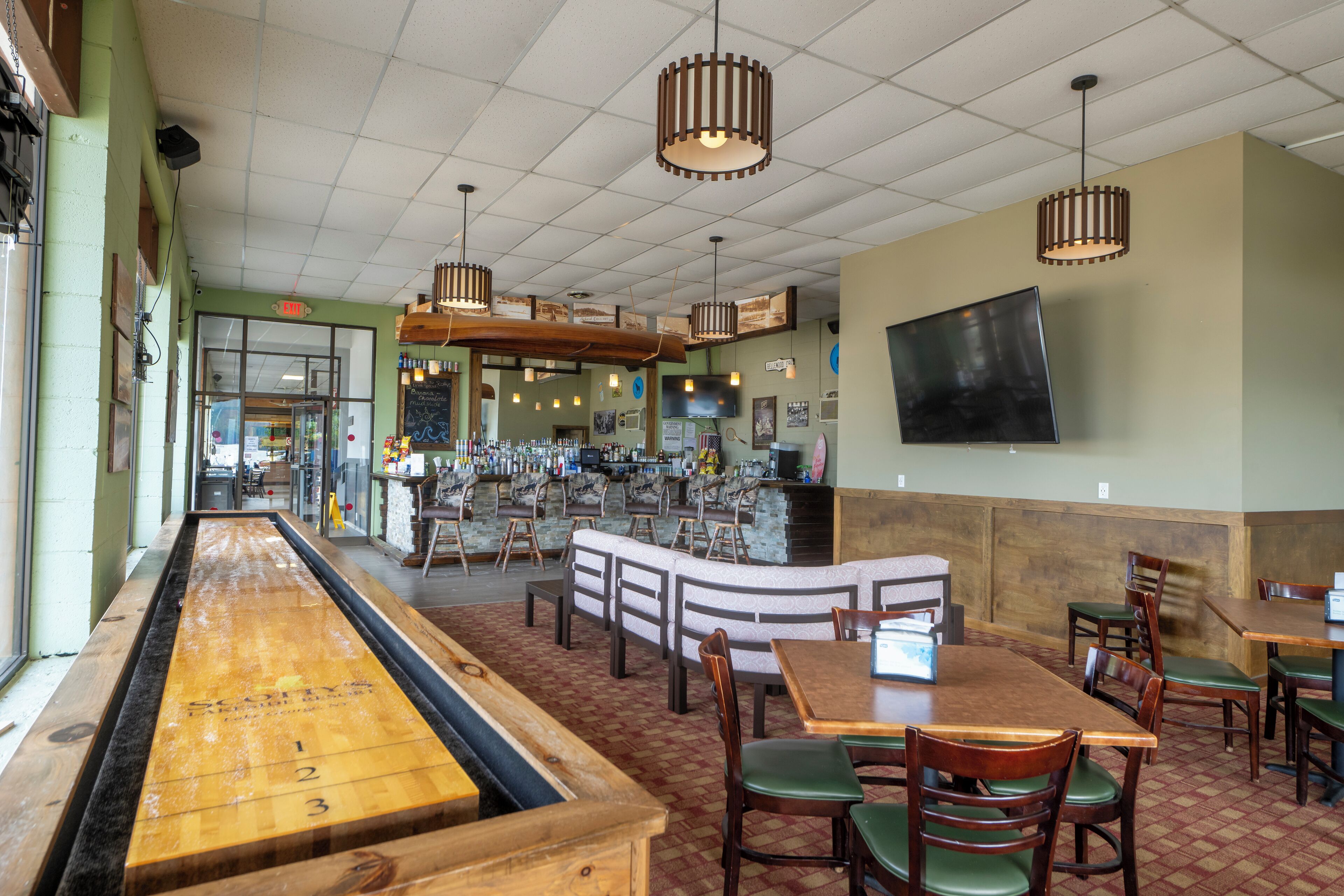 A restaurant with a long wooden table, booths, and a bar area.