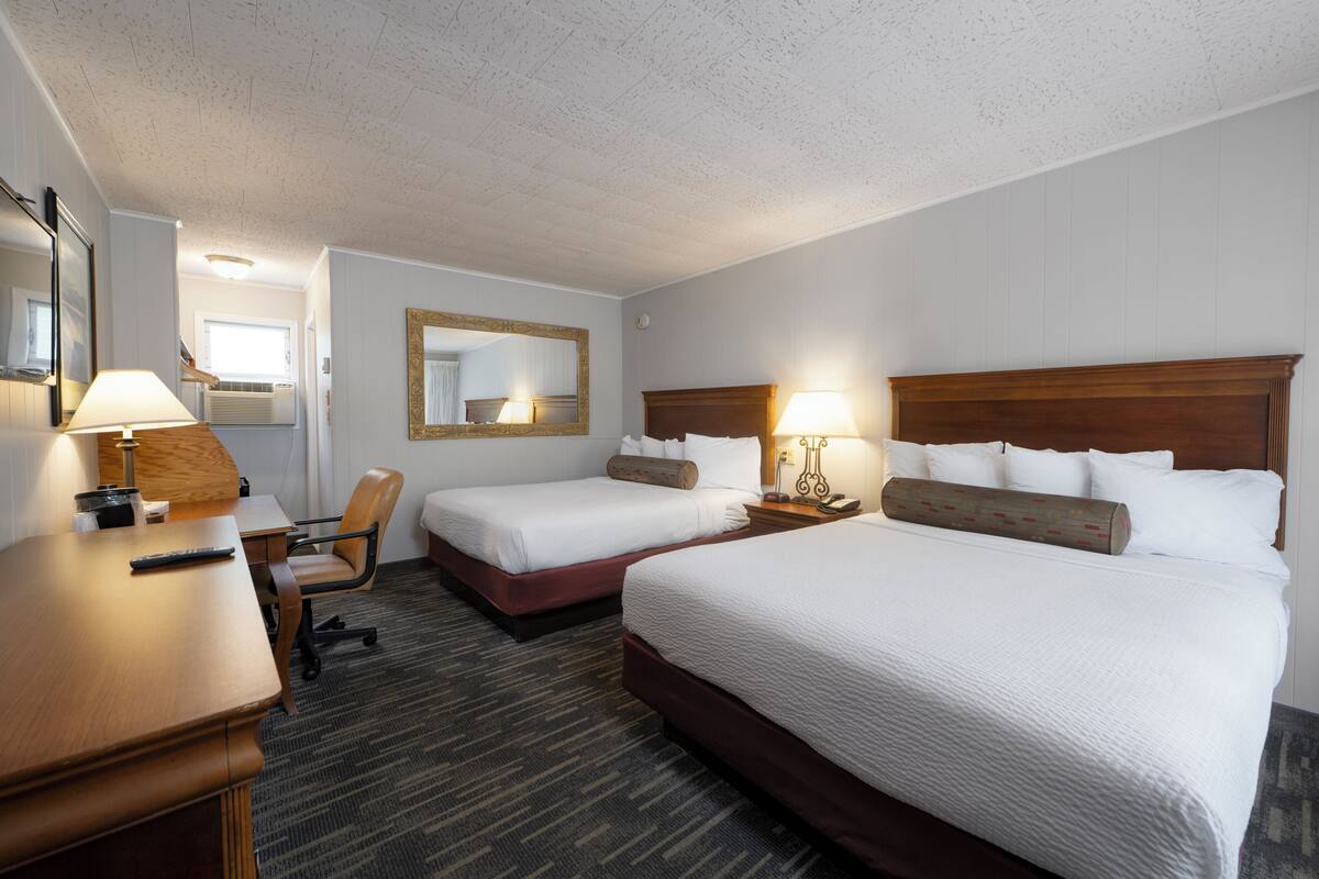 A hotel room with two beds, a desk, a chair, and a large mirror.
