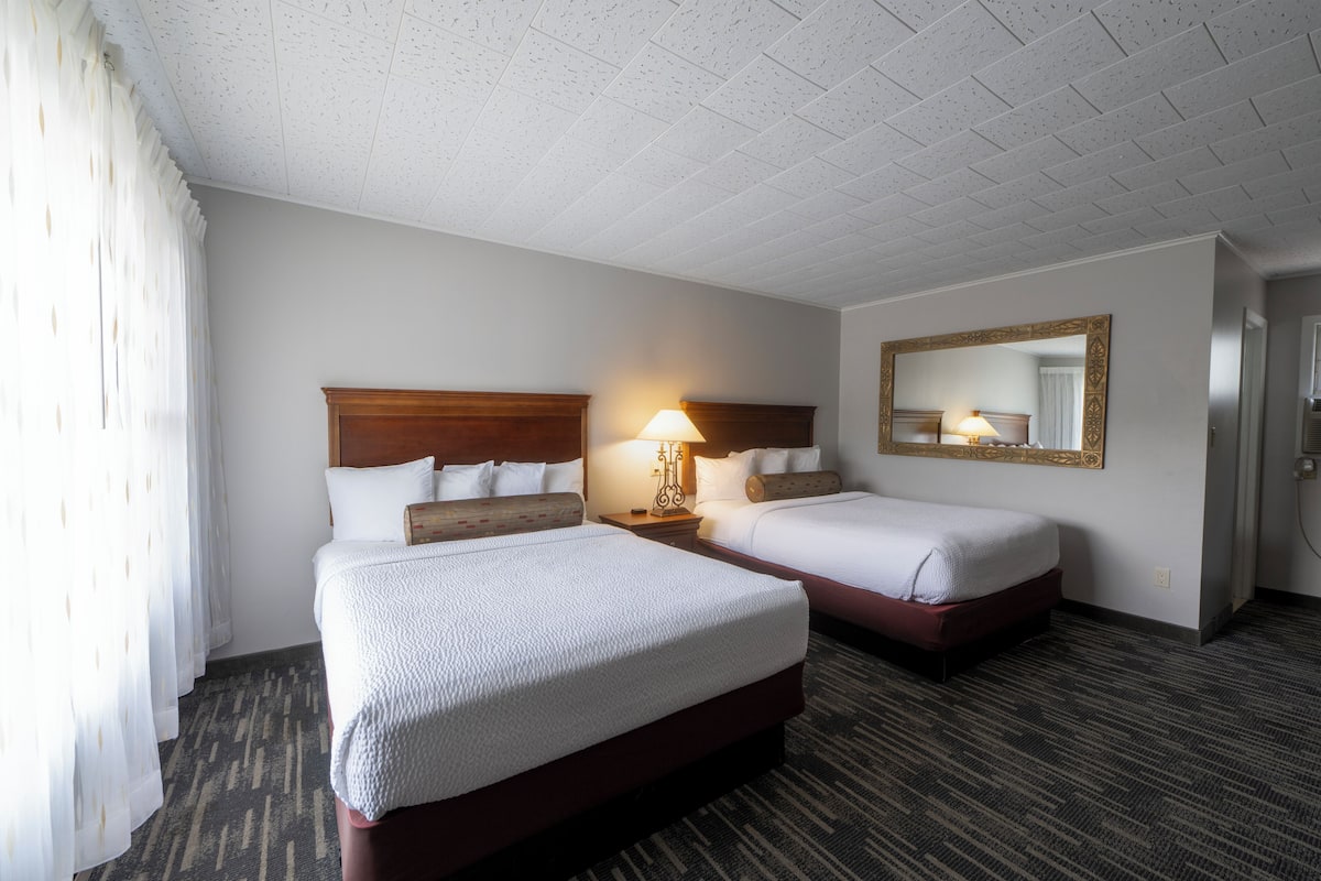 A hotel room with two beds, a large mirror, and a carpeted floor.