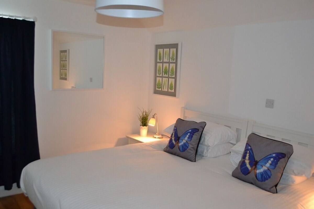 A neatly made bed with two pillows, a bedside lamp, and a small potted plant on a bedside table.