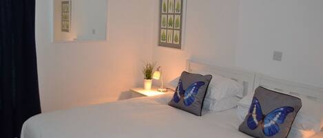 Una cama bien hecha con dos almohadas, una lámpara de noche y una pequeña planta en una mesita de noche.