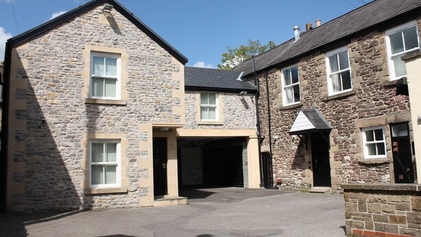 A stone building with a garage entrance, multiple windows, and a clear sky. - The Queens Head Hotel (Buxton)