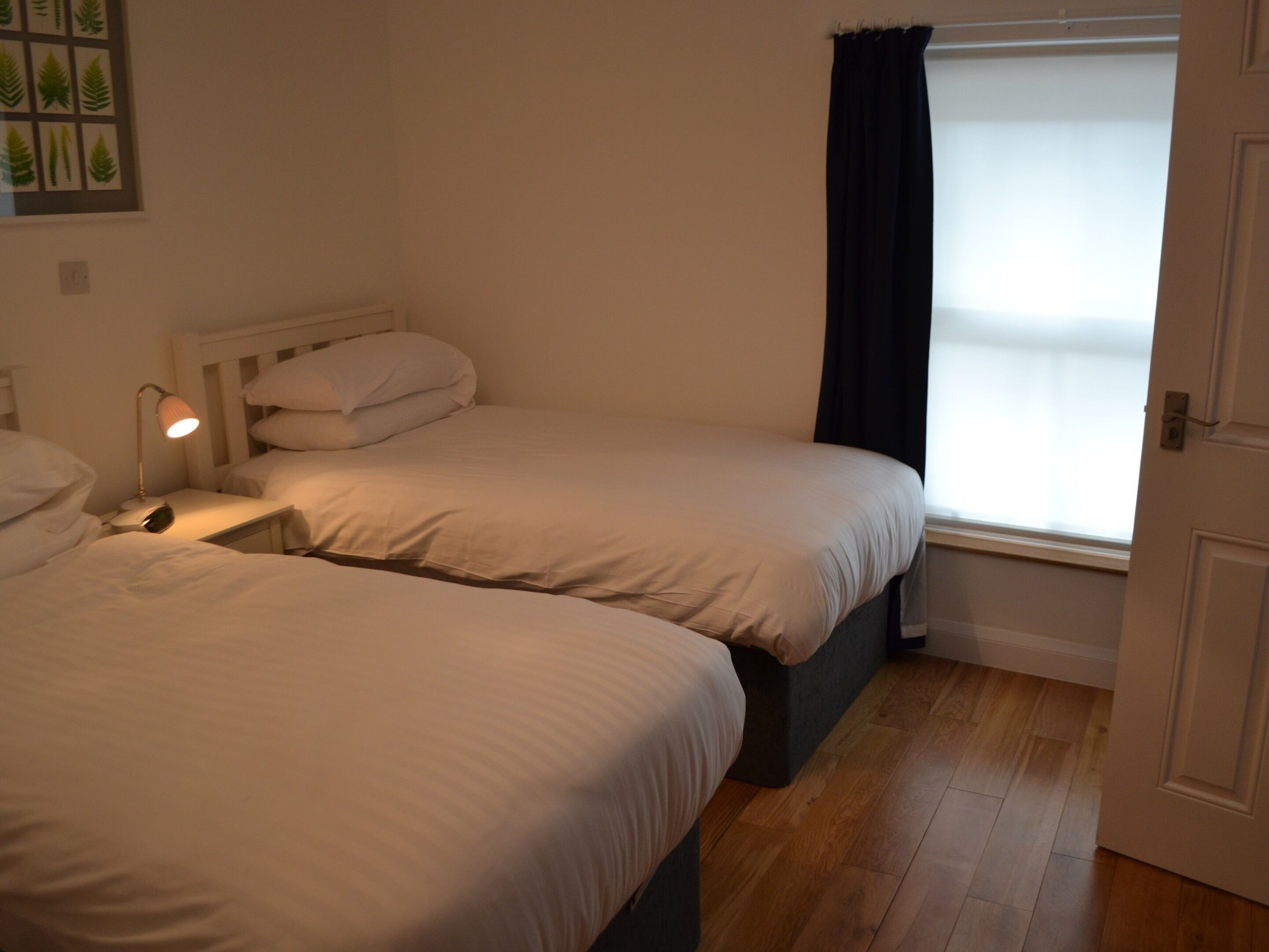 A bedroom with two beds, a bedside table with a lamp, and a window with curtains.