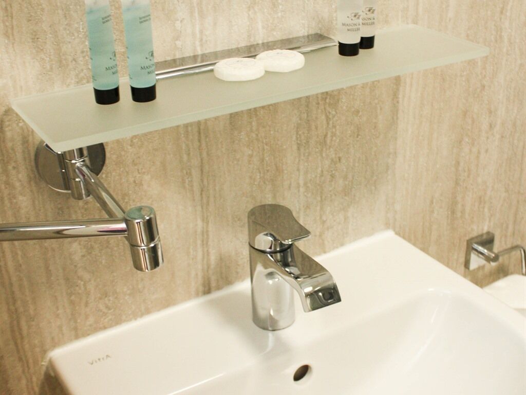 Un bagno con lavandino bianco, rubinetteria cromata e ripiano in vetro con articoli da toilette.