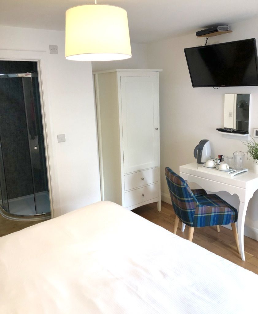 A hotel room with a bed, a desk with a chair, a television, and a wardrobe.