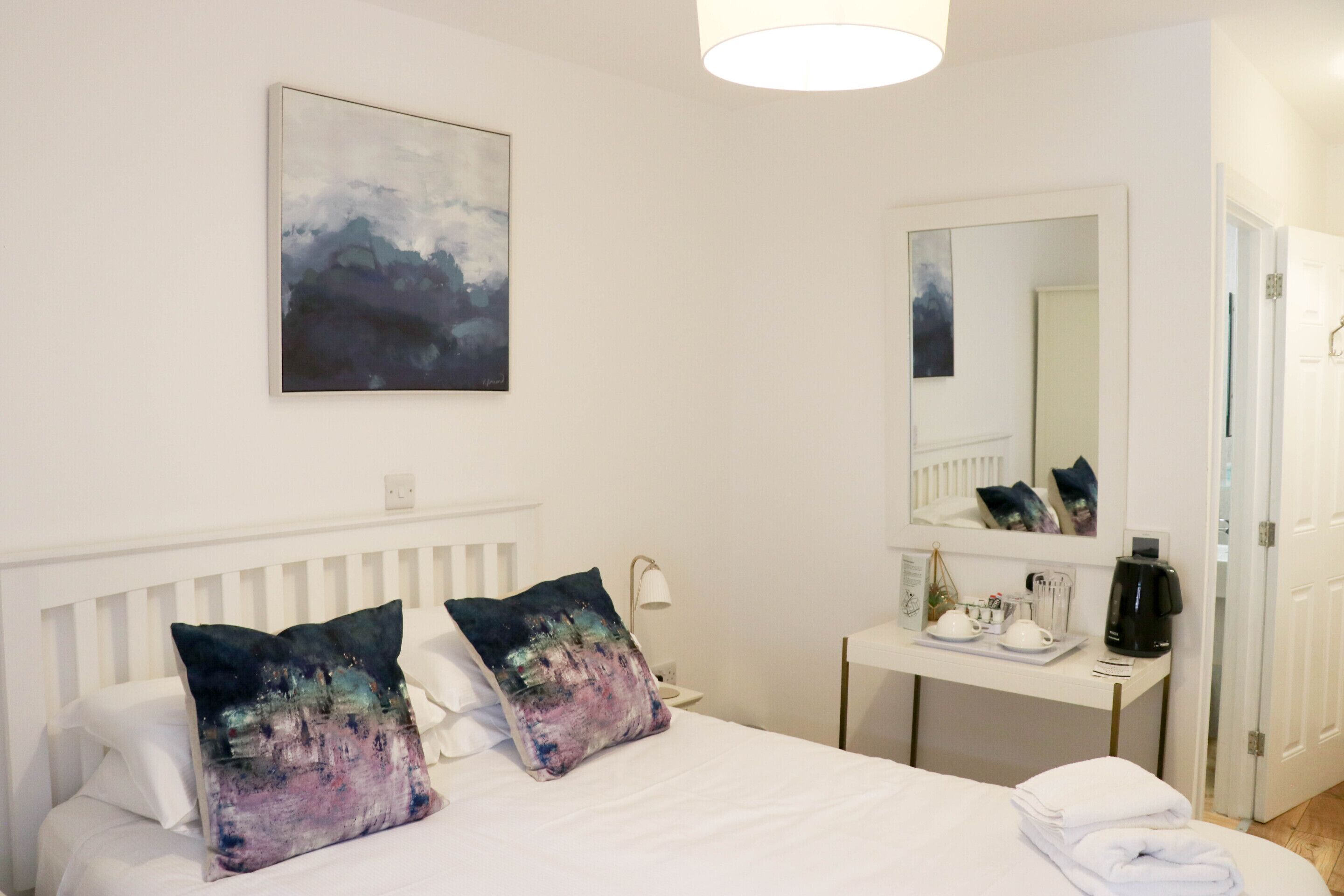 A hotel room with a bed, a bedside table with a lamp, a mirror, and a door.