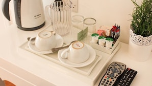 A kitchen counter with a coffee maker, two cups, a glass, a tray with condiments, and a remote control. - The Queens Head Hotel (Buxton)