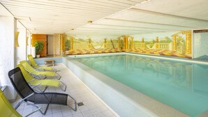 An indoor swimming pool with checkered tiles, yellow lounge chairs, and a mural of a landscape with columns.
