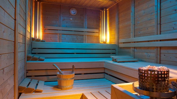 A wooden sauna with benches, a bucket, and a polka-dotted container.