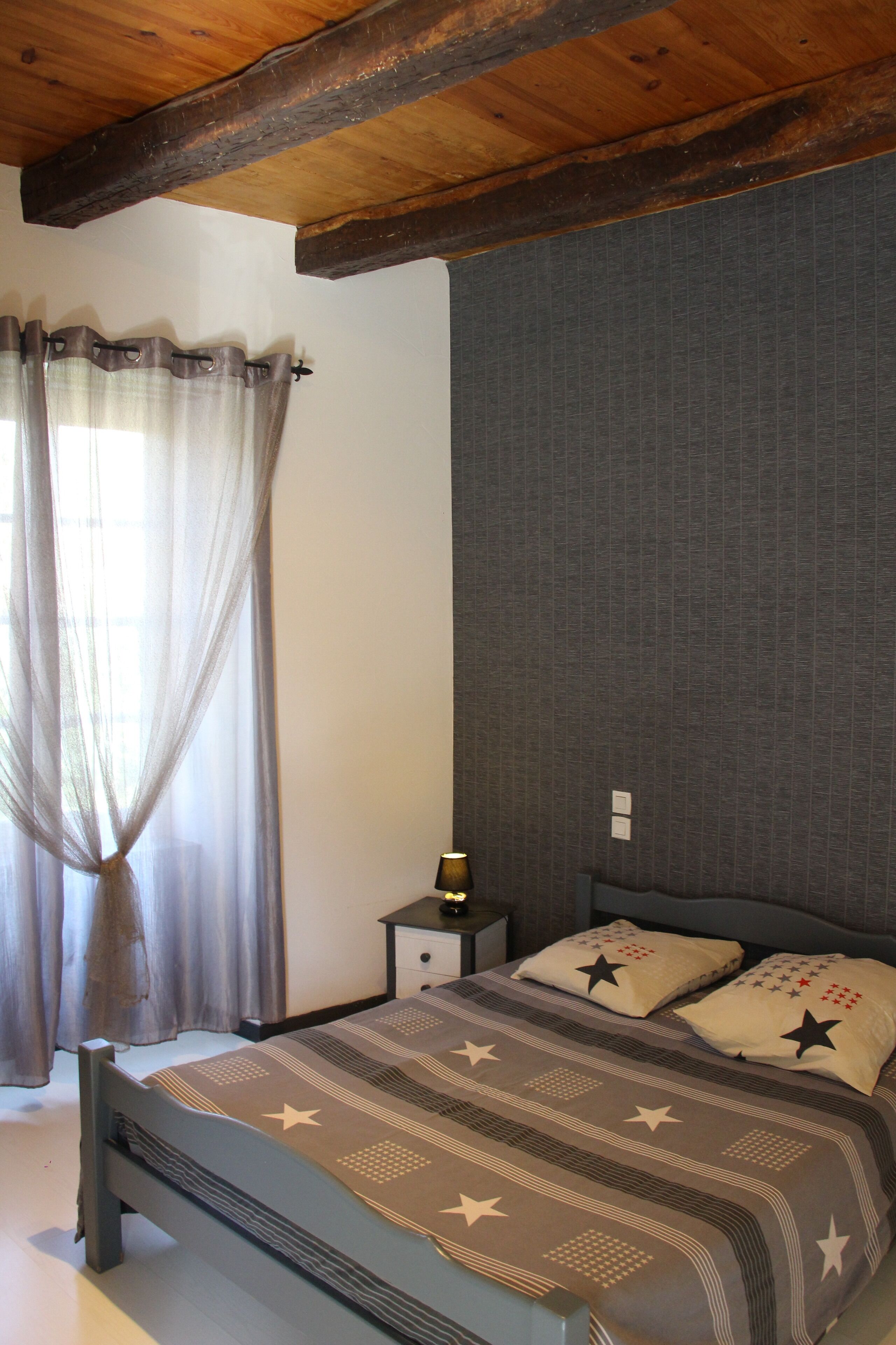 Un dormitorio con cama, cortinas, una mesita de noche y una pared con textura.
