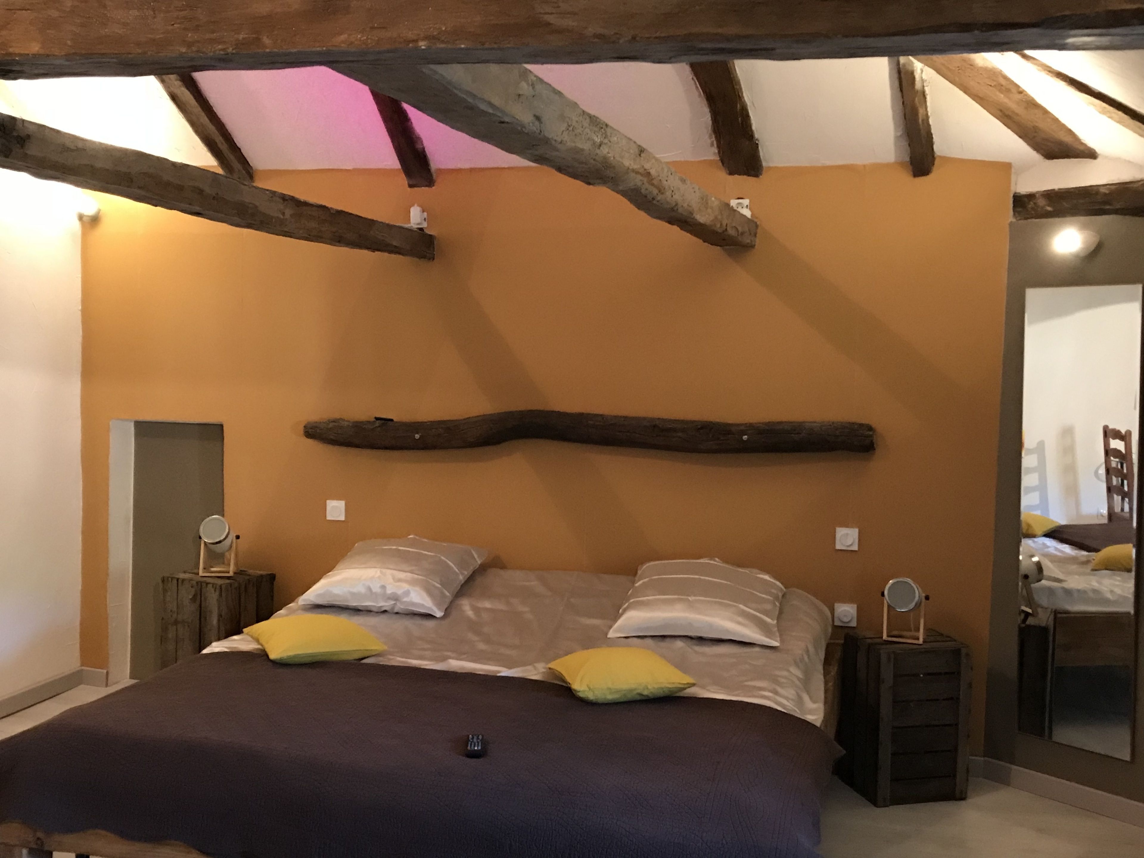Une chambre à coucher avec un lit, des poutres en bois, un miroir et une table de chevet.