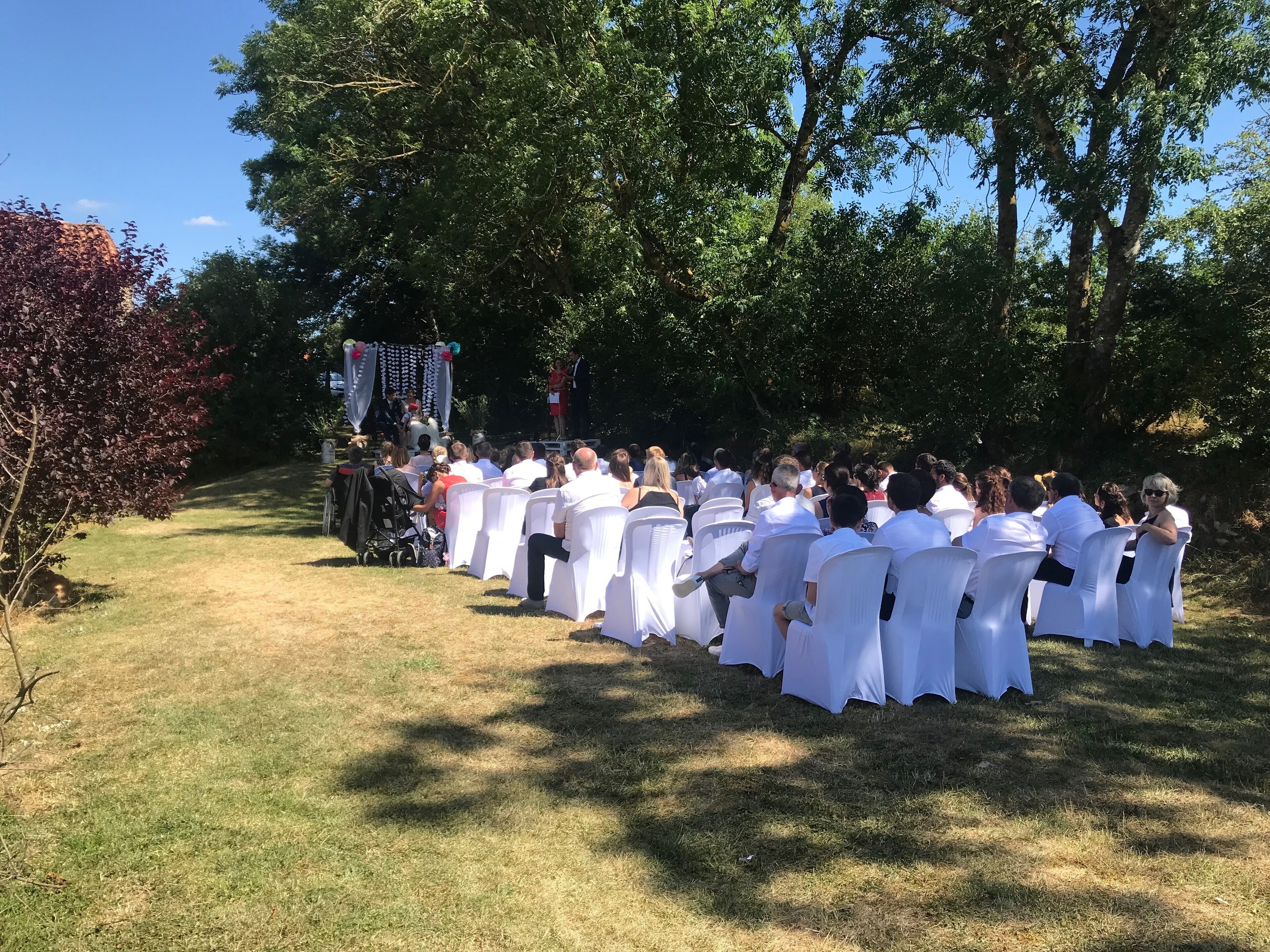 Ceremonia de boda al aire libre con invitados sentados en sillas blancas frente a un escenario decorado.