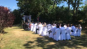 Ceremonia de boda al aire libre con invitados sentados en sillas blancas frente a un escenario decorado.