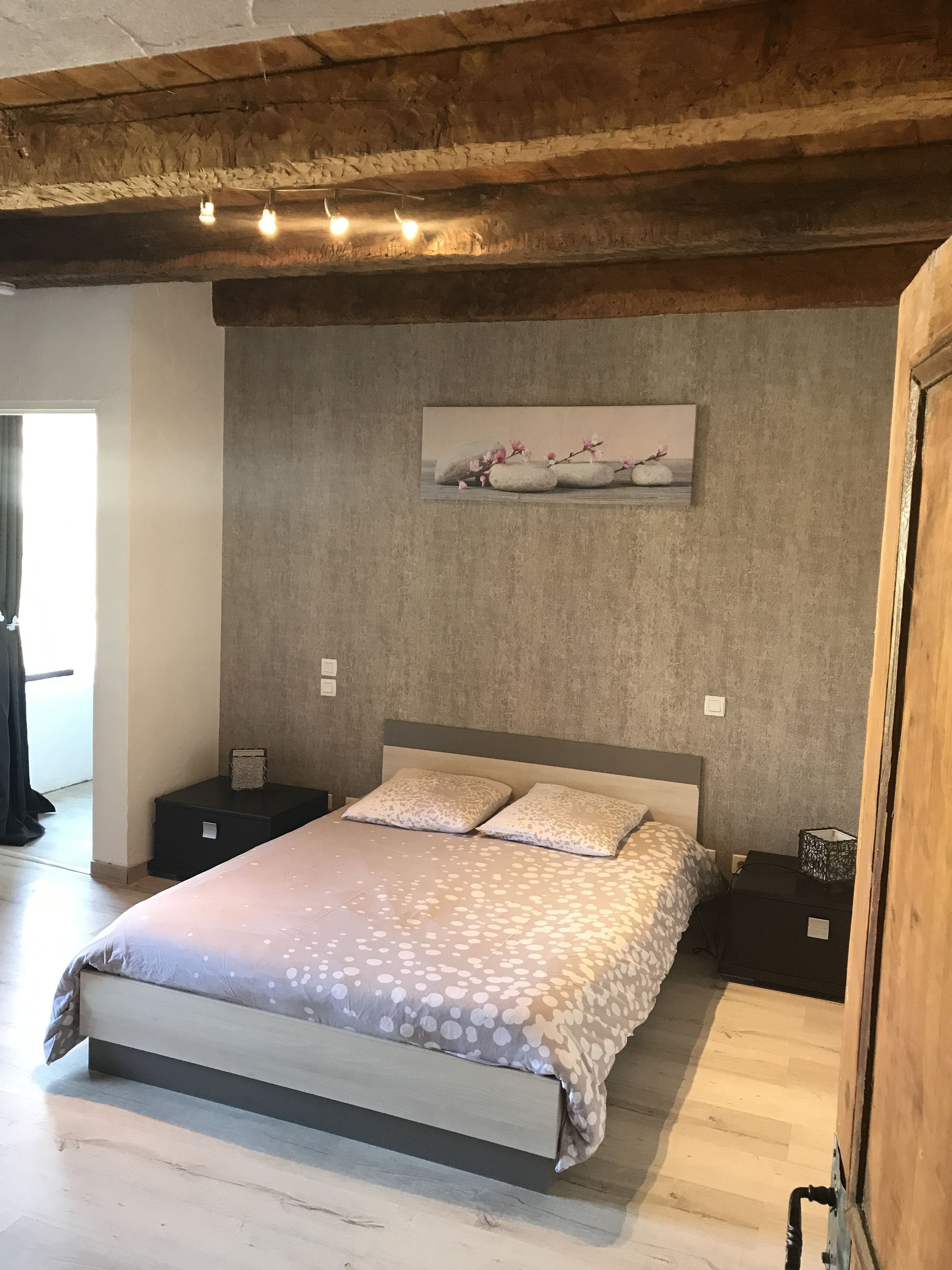 A bedroom with a bed, two bedside tables, a painting on the wall, and a wooden ceiling.