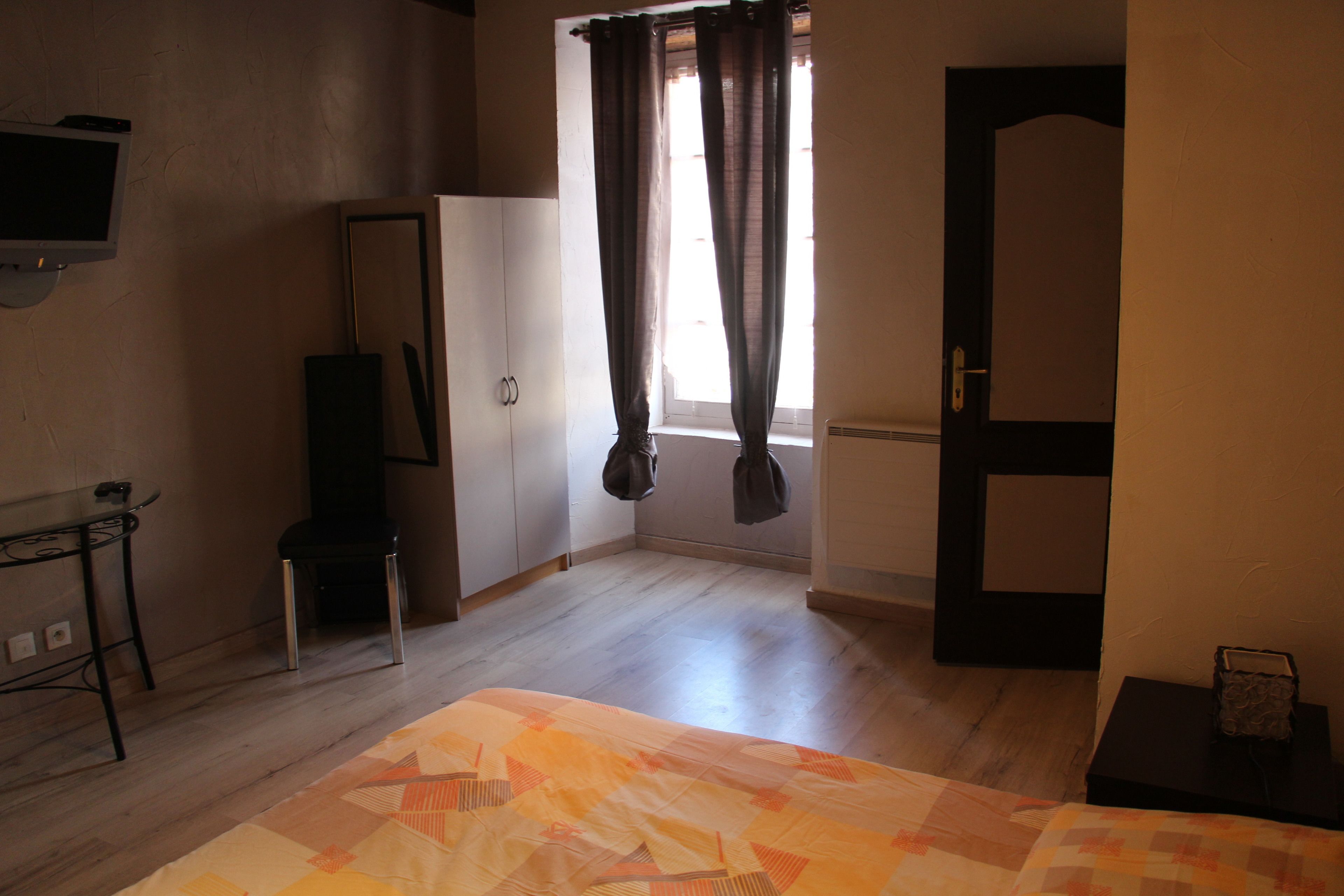 Une chambre avec un lit, un téléviseur fixé au mur, une armoire et une fenêtre avec des rideaux.
