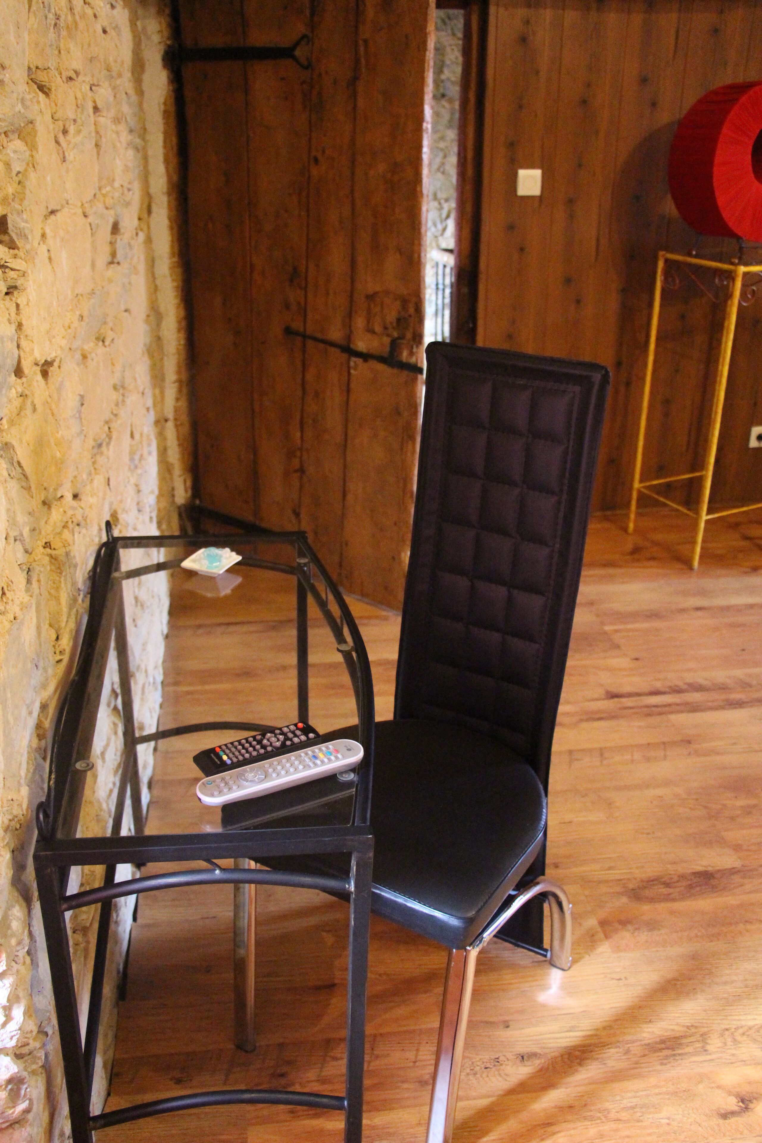A black upholstered chair with a glass table in front, a remote control on the table, and a wooden floor.