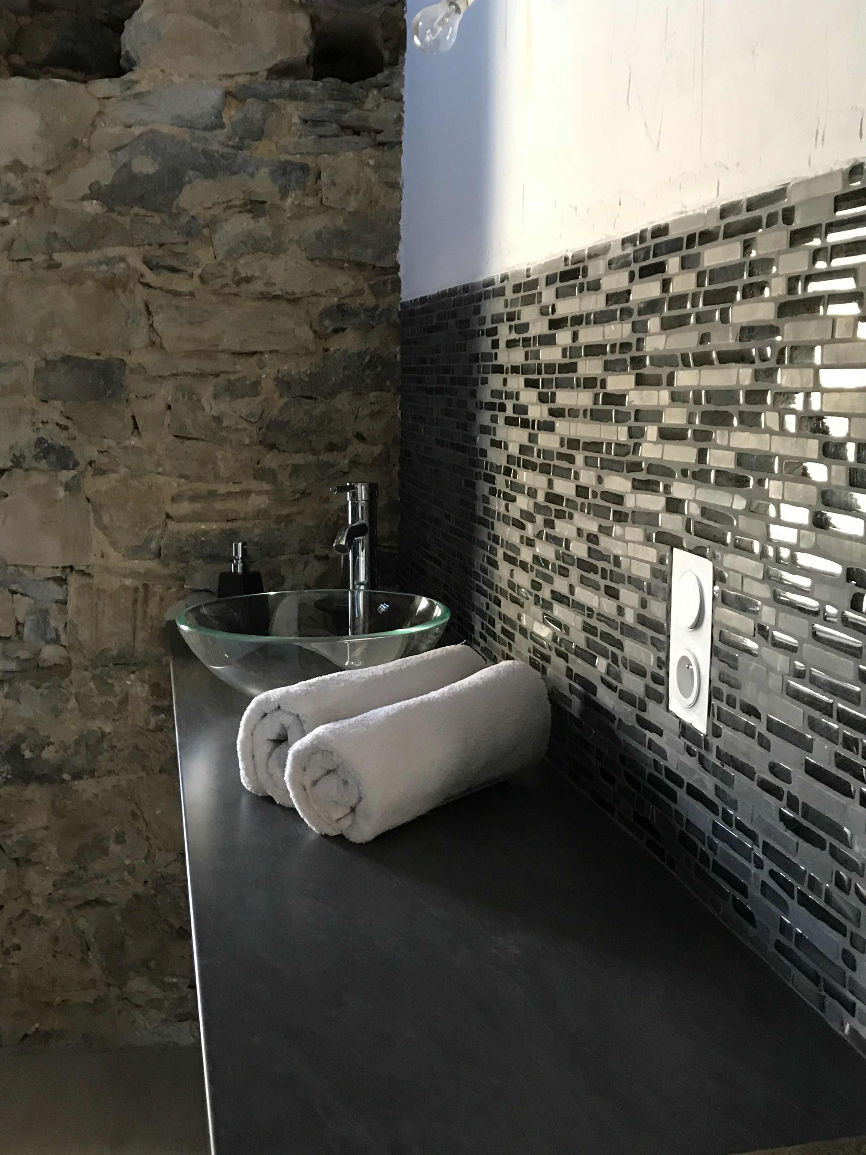 A bathroom with a stone wall, a glass sink, and a tiled backsplash.