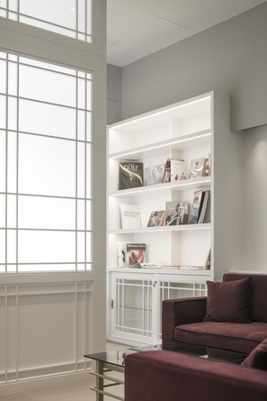 A modern living room with a white built-in bookshelf, a red sofa, and a glass coffee table. - Palazzo Castri 1874 Spa & Garden (Florence)