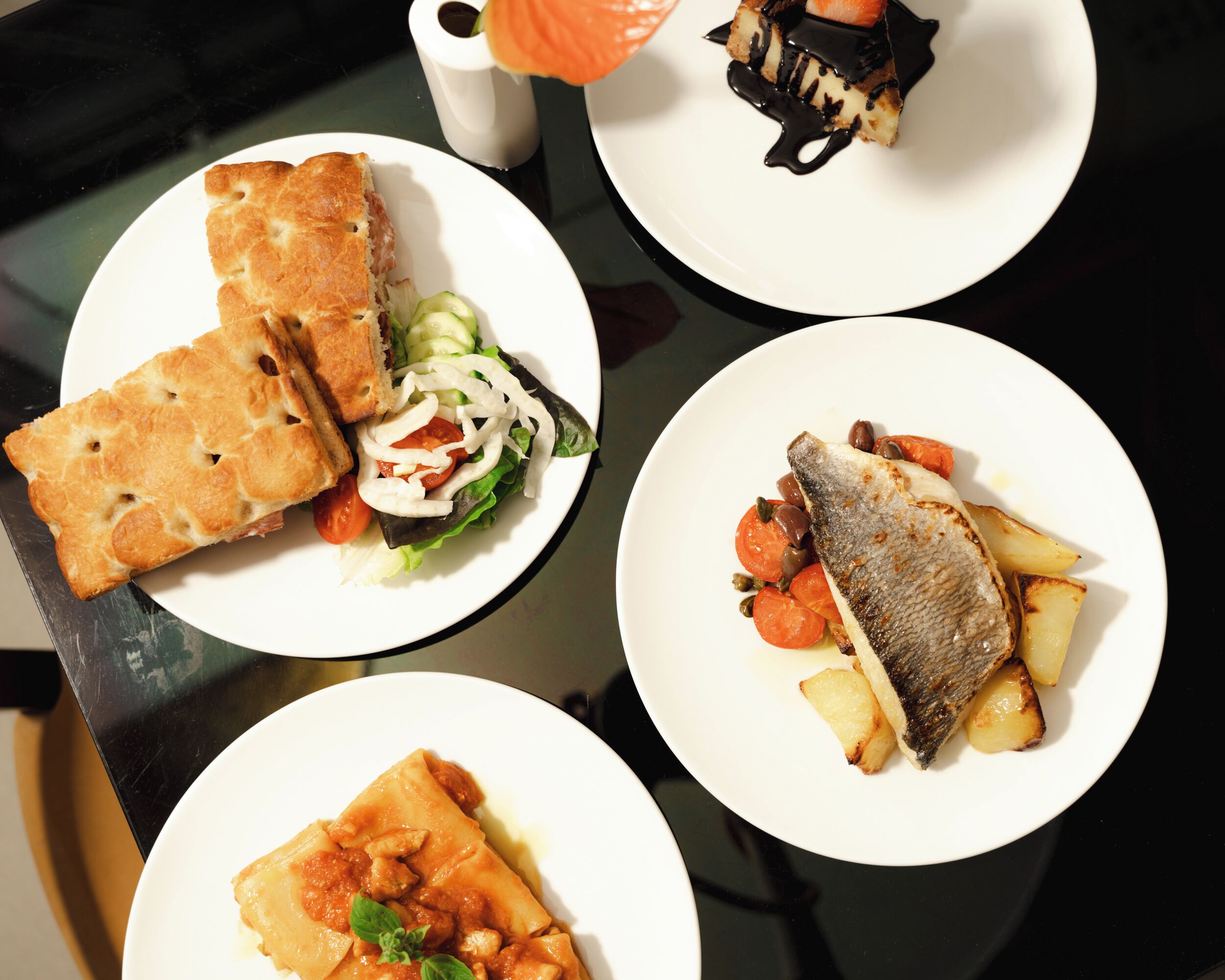A table with four plates of food, including a fish dish, a dessert, and a sandwich.