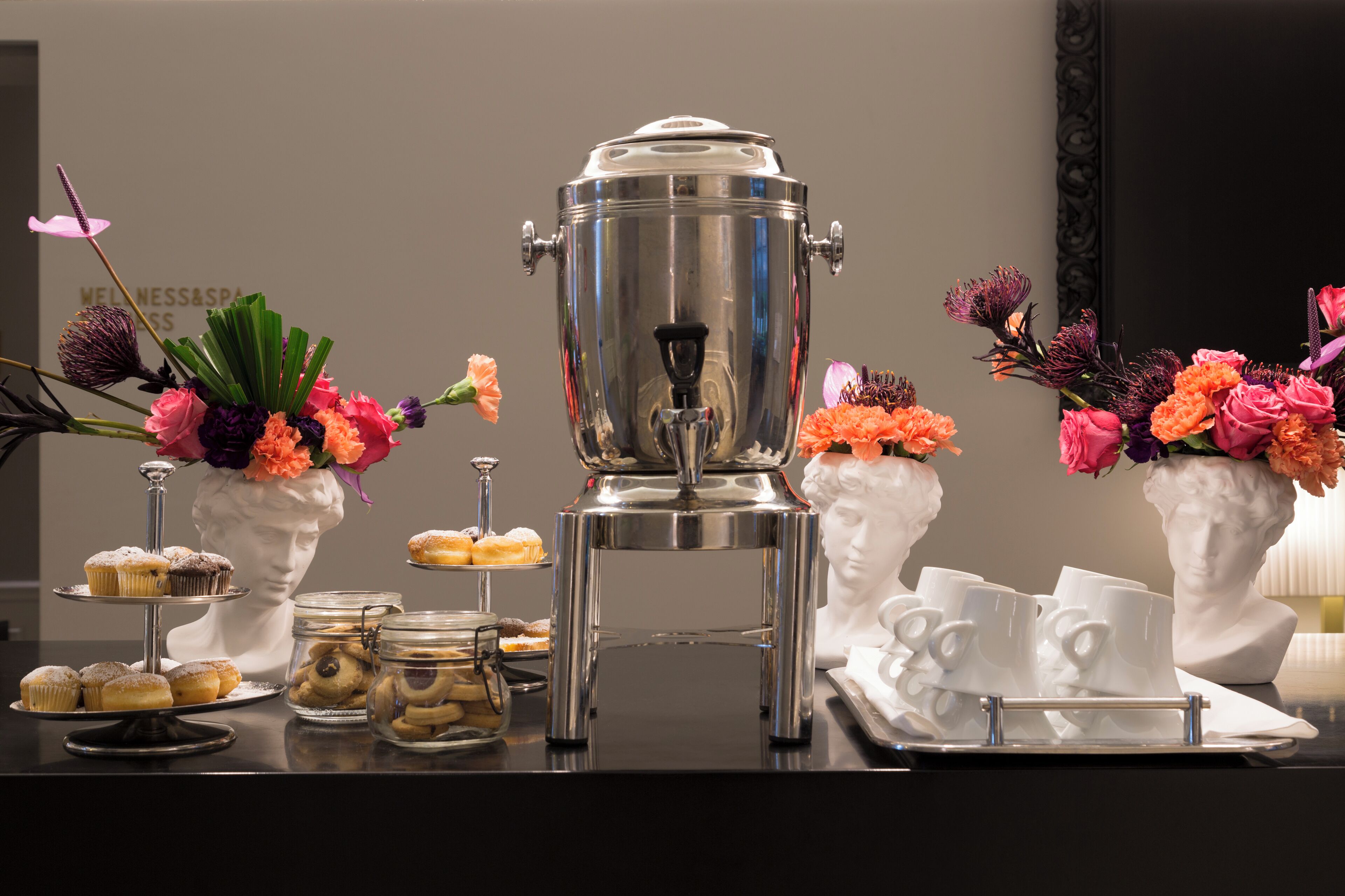 A buffet setup with a coffee pot, pastries, and floral arrangements.