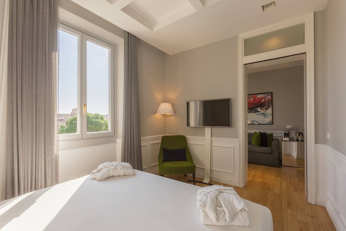 A hotel room with a large bed, a TV, a green chair, and a view of the city.