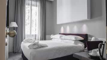 Habitación de hotel con cama, escritorio con hervidor, lámpara y ventana con cortinas.
