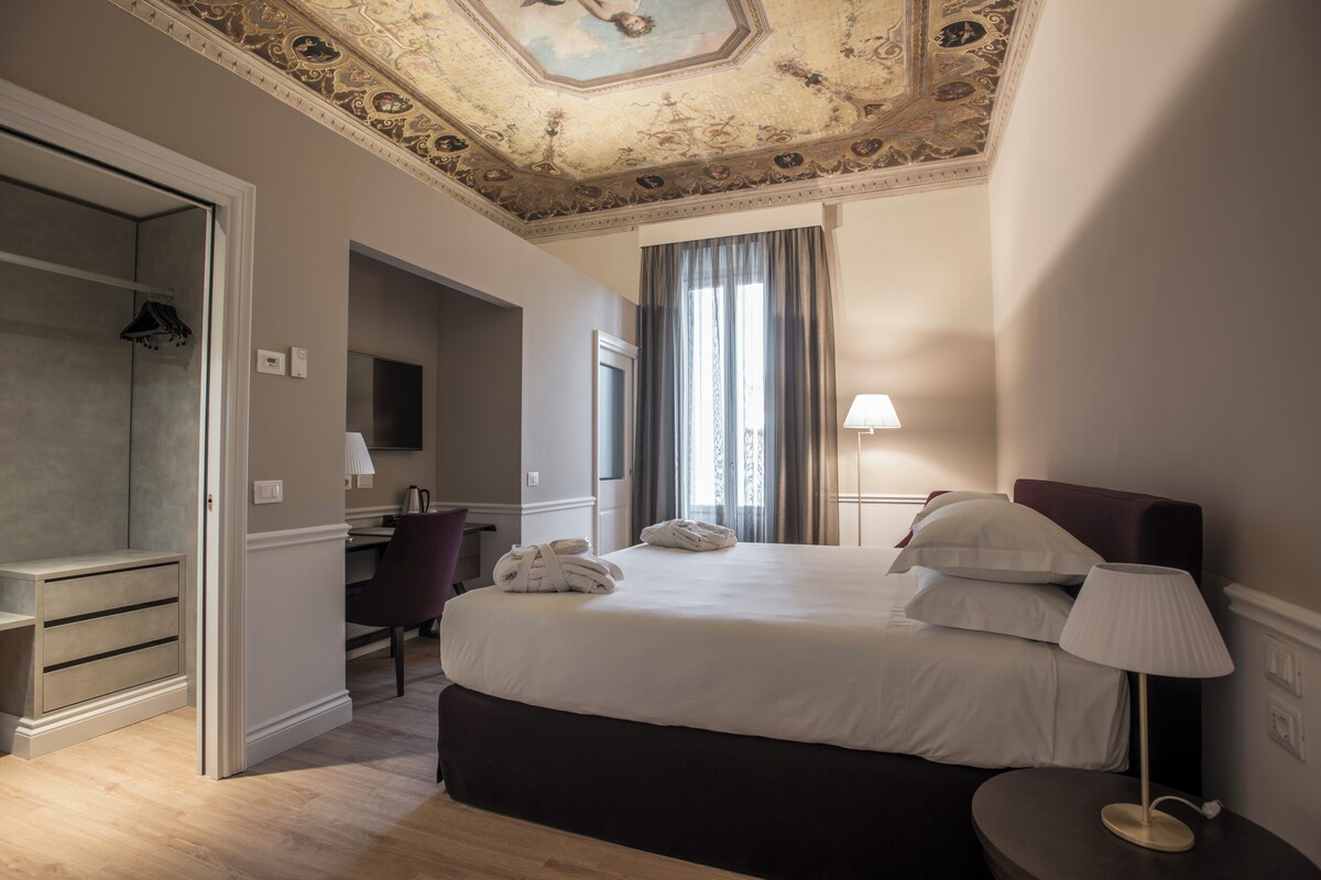 A hotel room with a bed, a desk, a chair, a wardrobe, and a bathroom.
