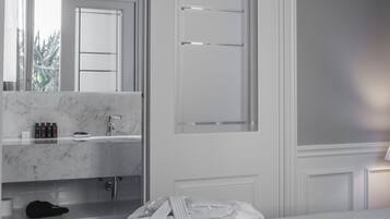 A hotel room with a marble bathroom vanity, a bed, and a view of greenery outside.