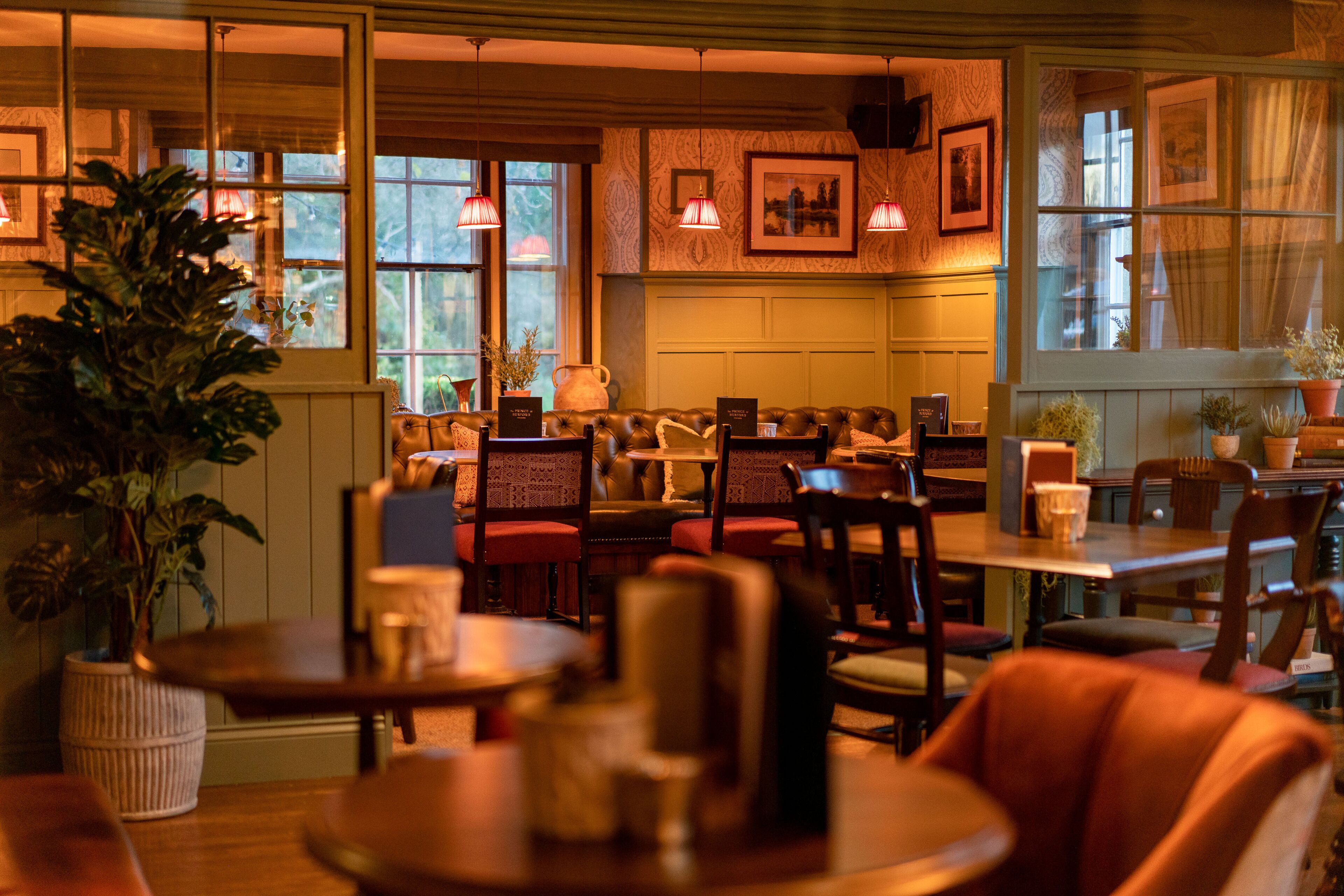 Un restaurante acogedor con mobiliario de madera, ventanas amplias y plantas en macetas.