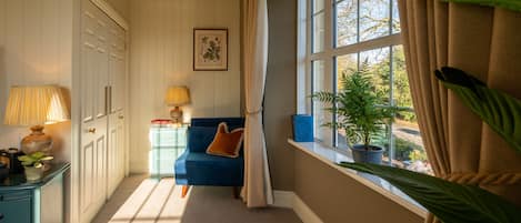 A room with a blue sofa, a window with curtains, a lamp, and a plant.