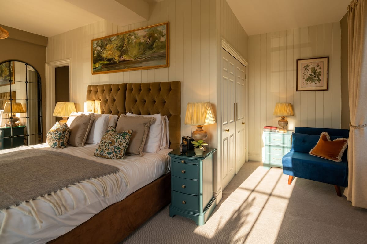 A bedroom with a large bed, bedside tables, a blue armchair, and a wardrobe.