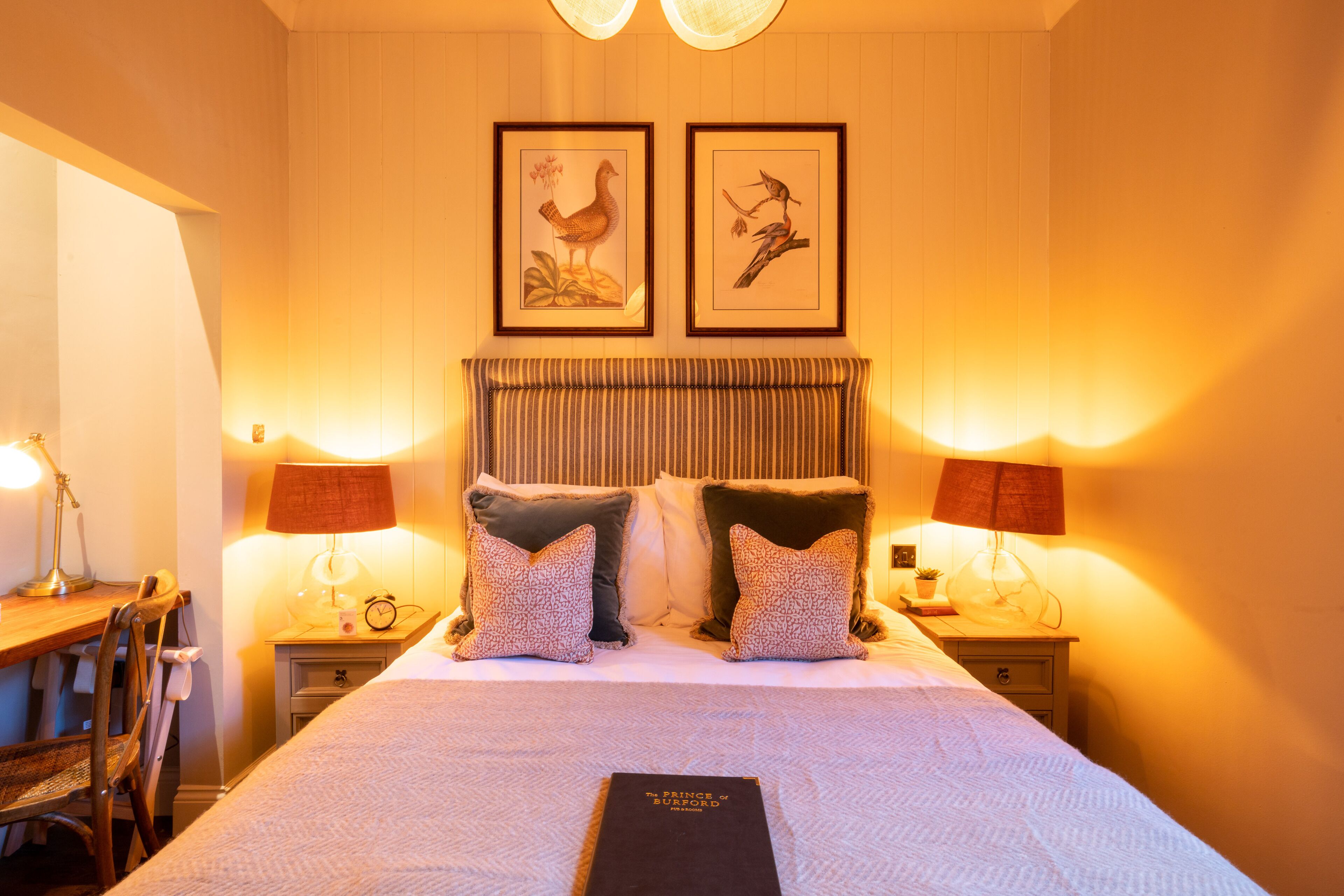 Een keurig opgemaakt slaapkamer met een groot bed, twee nachtkastjes met lampen, een stoel en lijstwerken aan de muur.