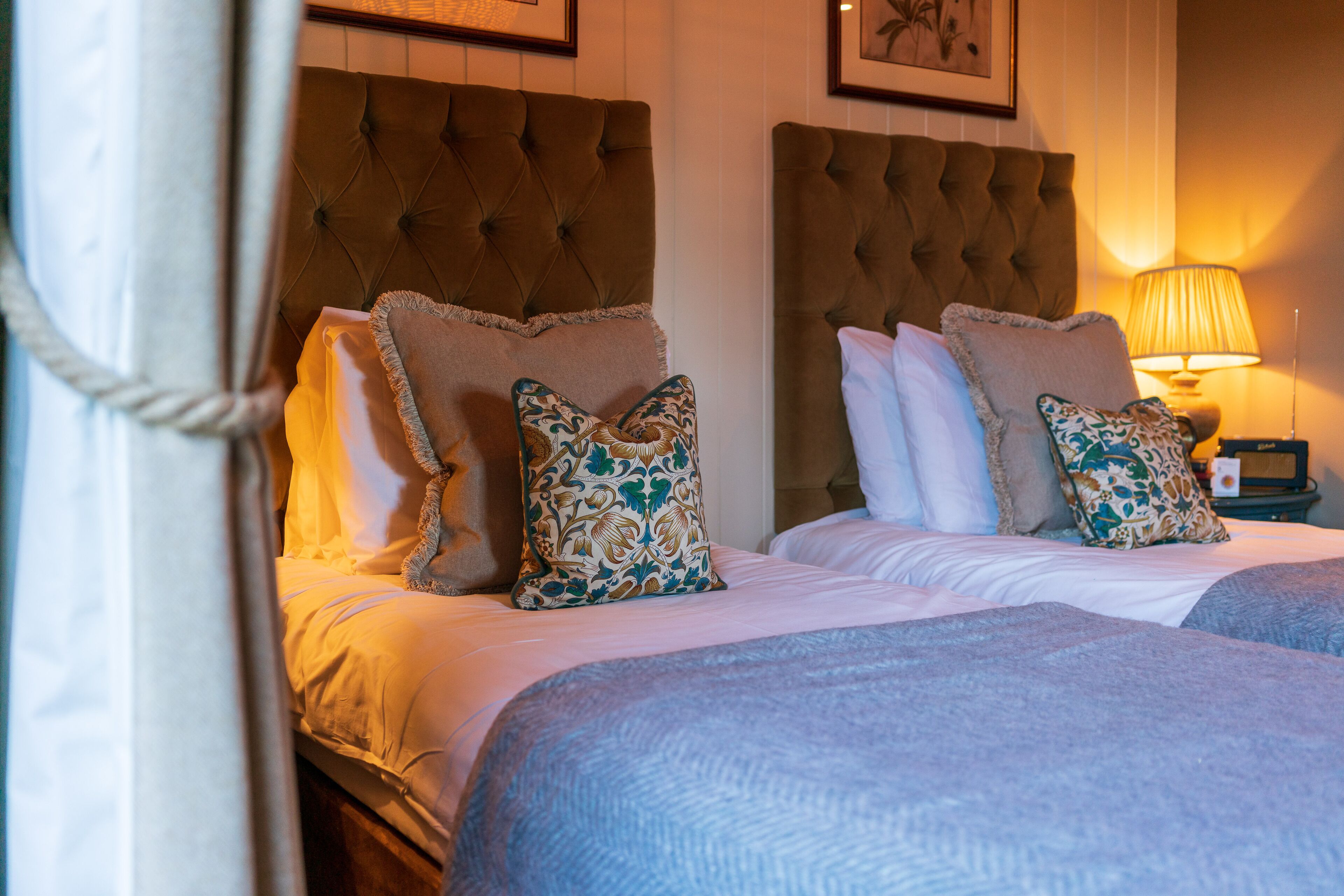 A hotel room with two beds, each with a tufted headboard, white linens, and patterned throw pillows.