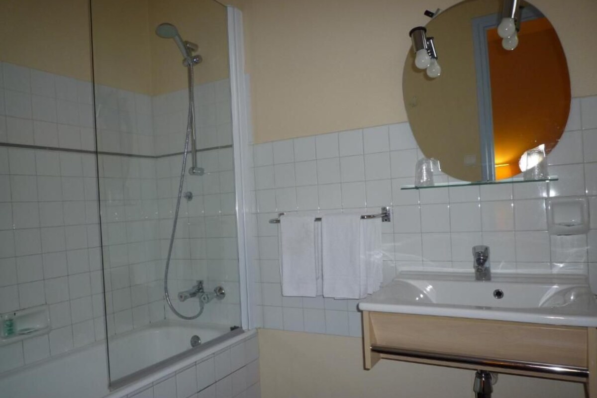 A bathroom with a glass-enclosed shower, a sink with a mirror, and white tiled walls.