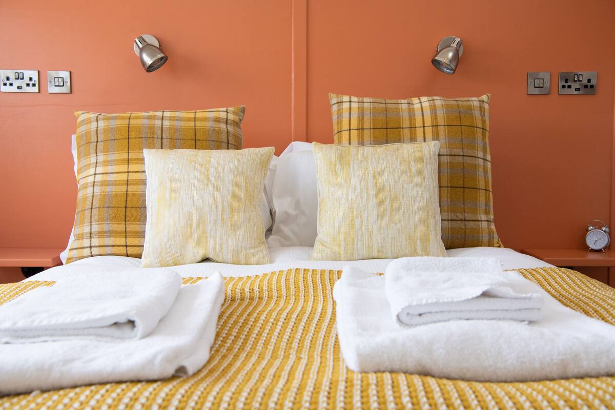 A neatly made bed with yellow and white bedding, two pillows, and two folded towels.