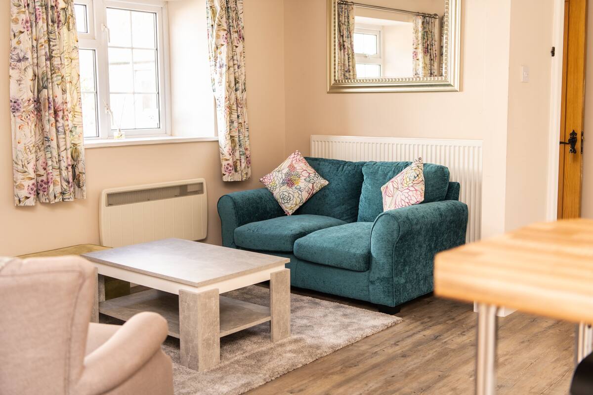 A cozy living room with a teal sofa, a white coffee table, and a floral curtain.