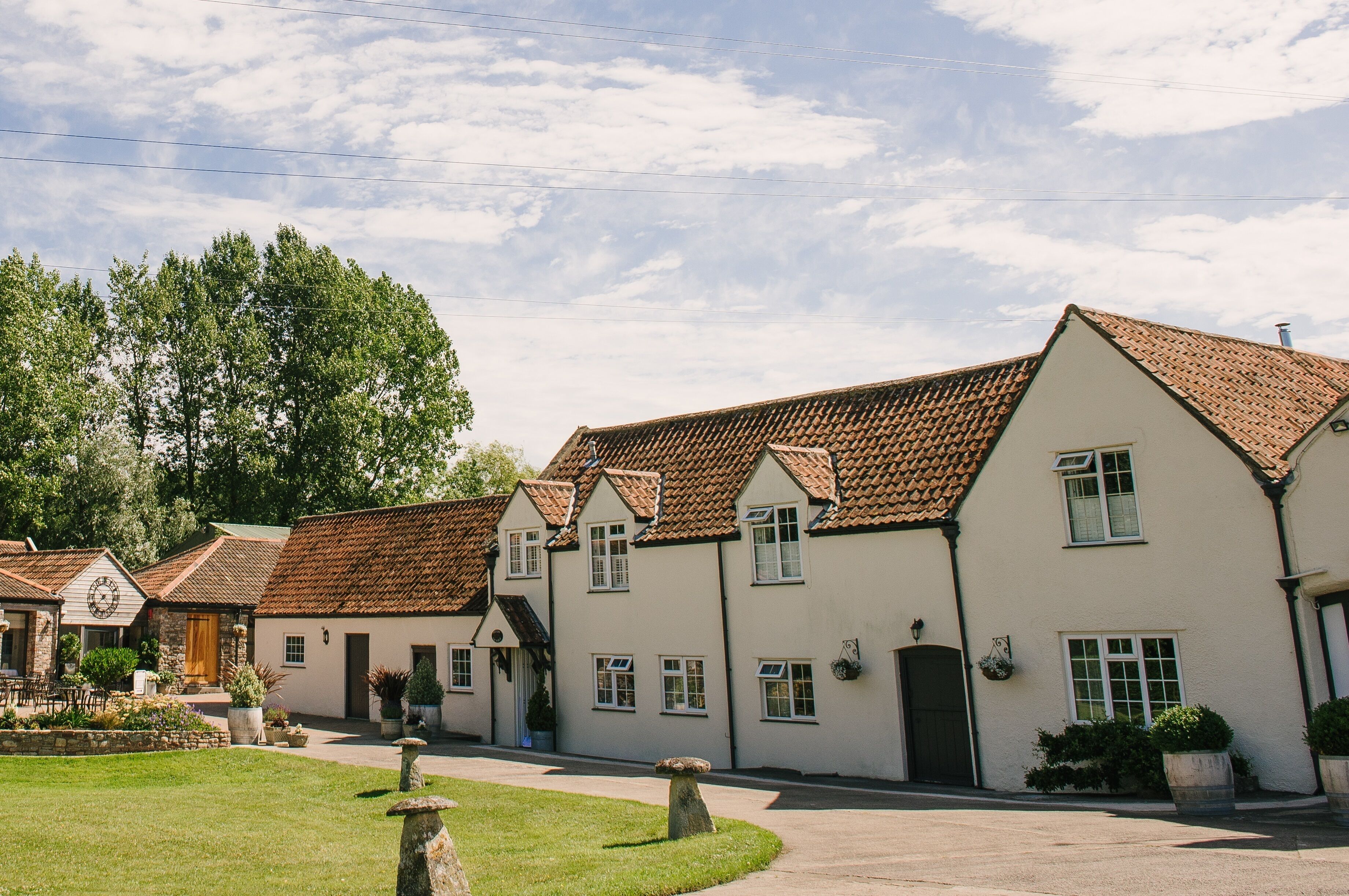 A row of white buildings with brown tiled roofs, a stone pathway, and a grassy area with a stone bench.