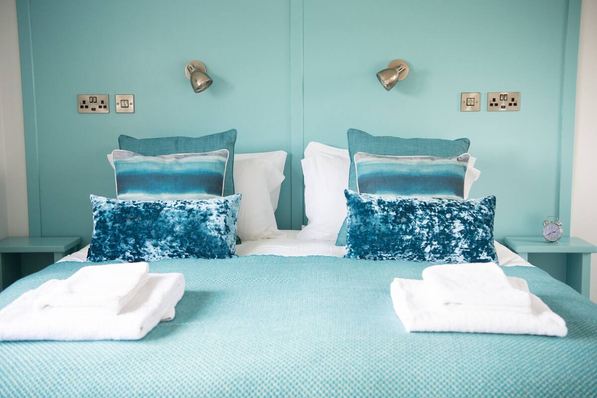 A double bed with a blue and white patterned bedspread, two matching pillows, and two white towels folded on the bed.