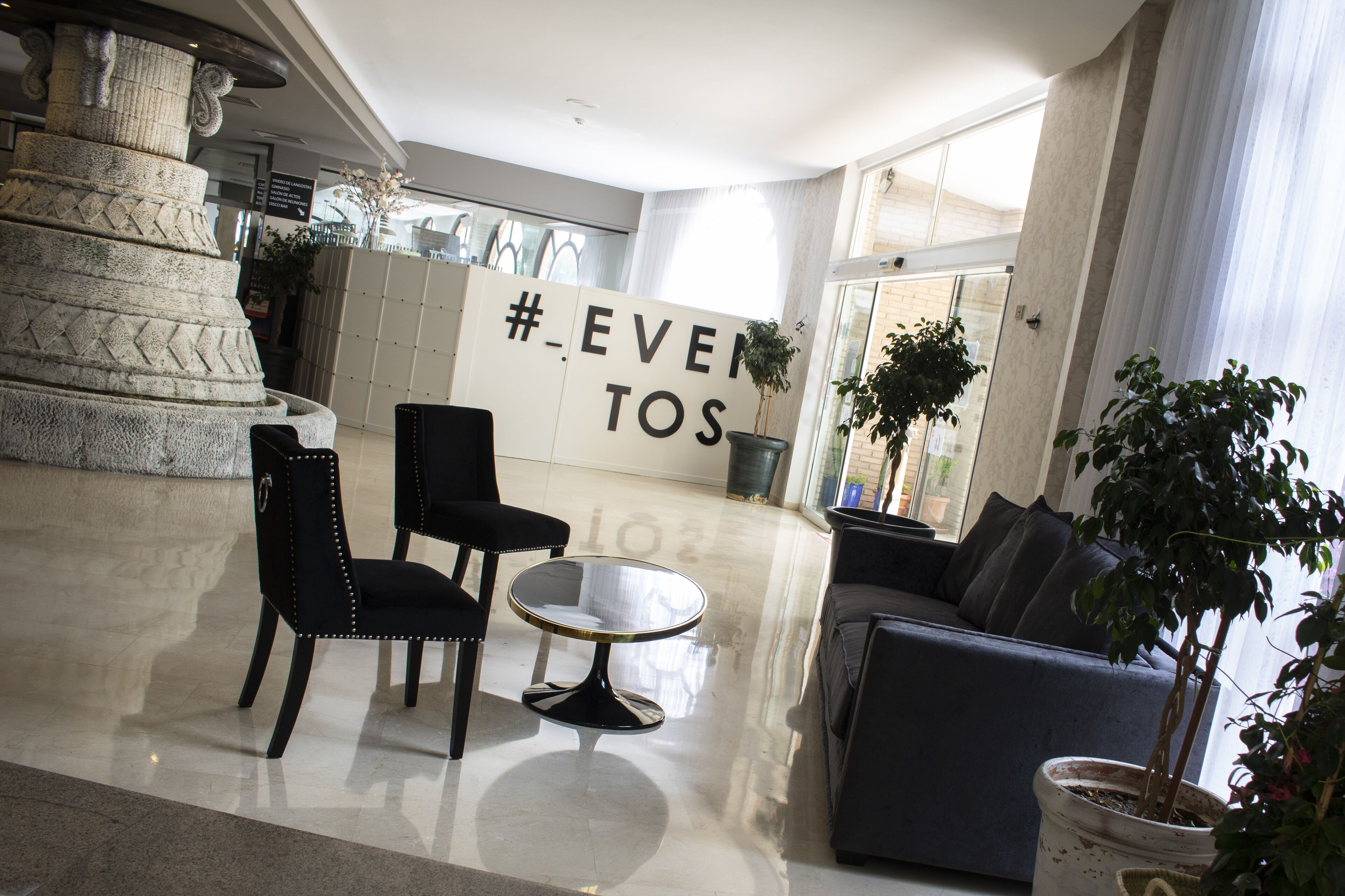 A modern lobby with a stone column, a seating area with a round table, and a sofa.