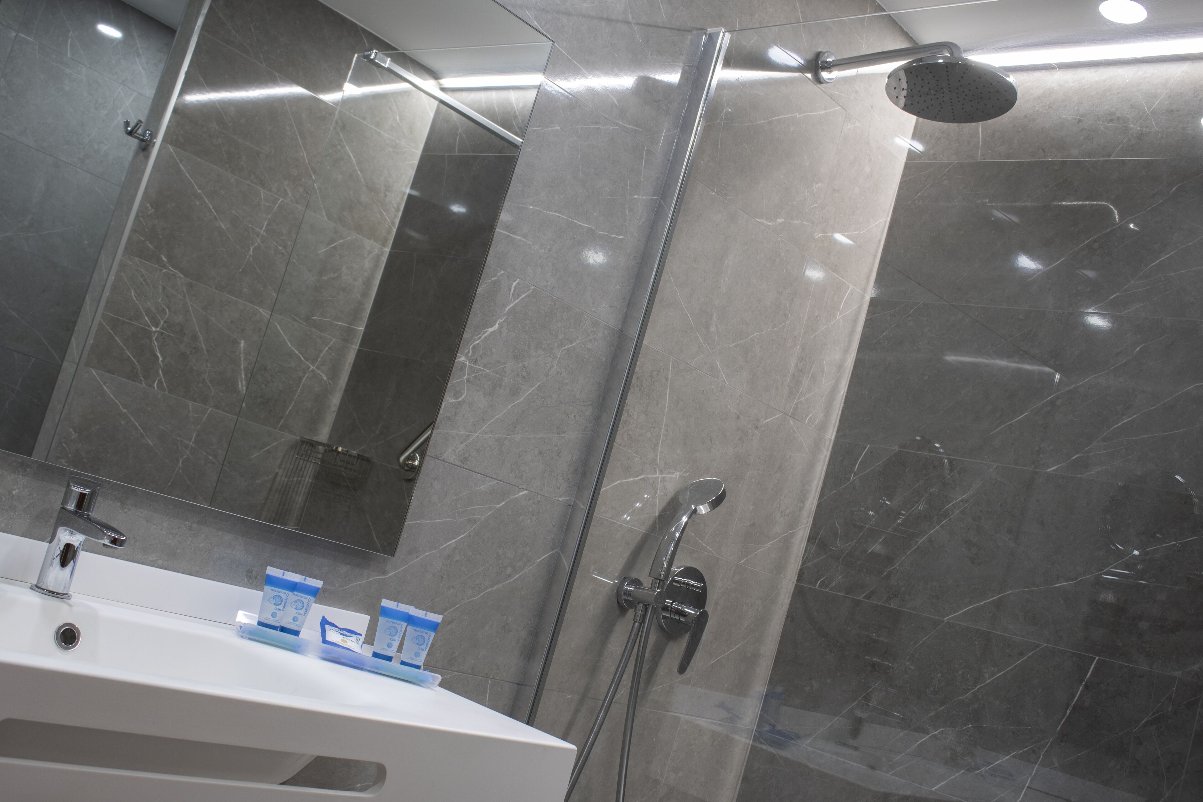 Un baño moderno con un espejo grande, un lavamanos y una ducha con cabezal de ducha manual.