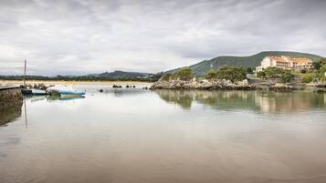 A calm waterfront with boats, a beach, and a hill with a building.