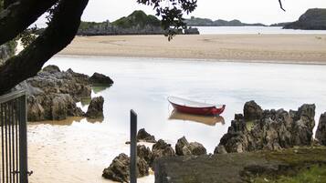 A beach with a red boat anchored near rocks and a sandy shore.