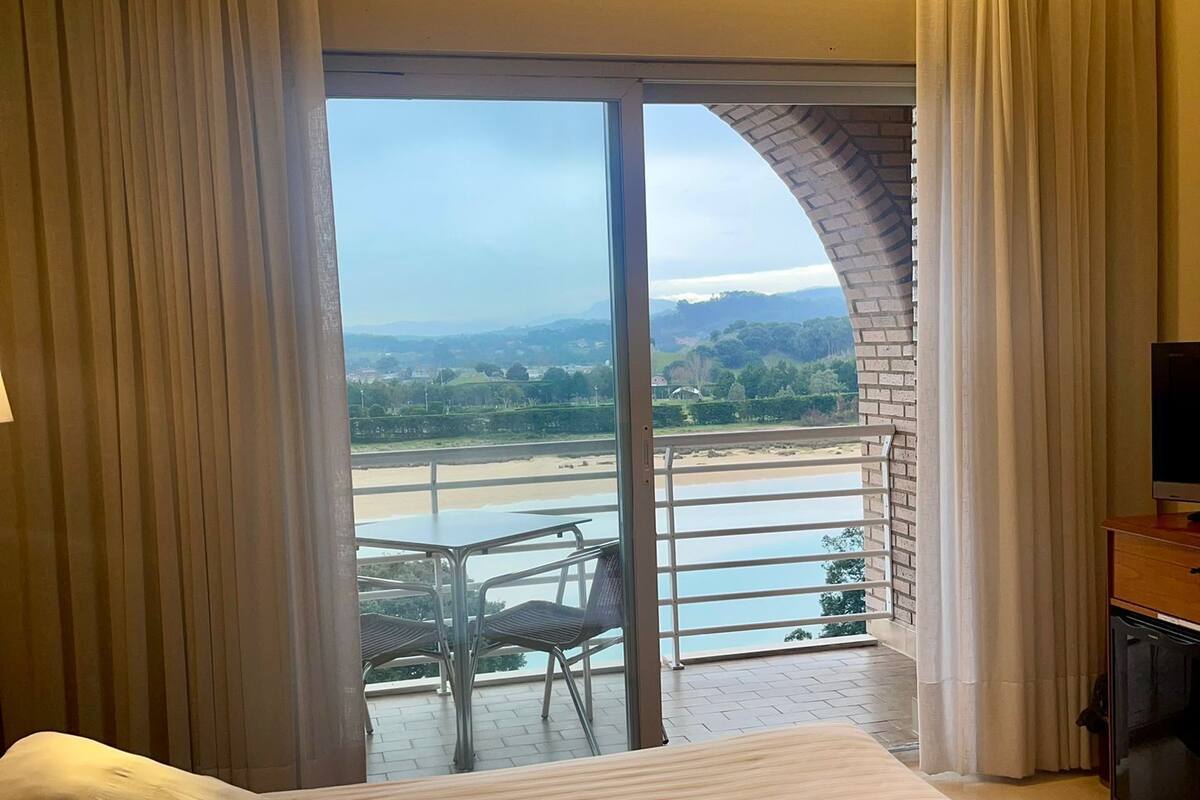 Une chambre d’hôtel avec un grand lit, une télévision et un balcon offrant une vue sur la plage et les montagnes.