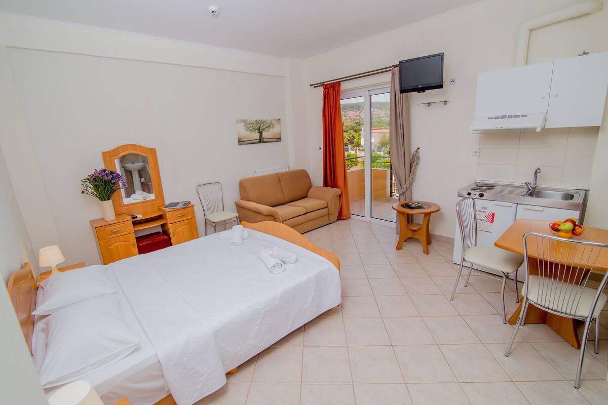 Ein Hotelzimmer mit Bett, einer Sitzecke, einer kleinen Küchenzeile und einem Balkon mit Fernseher.
