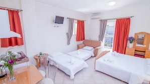 Habitación de hotel con dos camas individuales, una mesita con una silla, televisor y ventana con cortinas.
