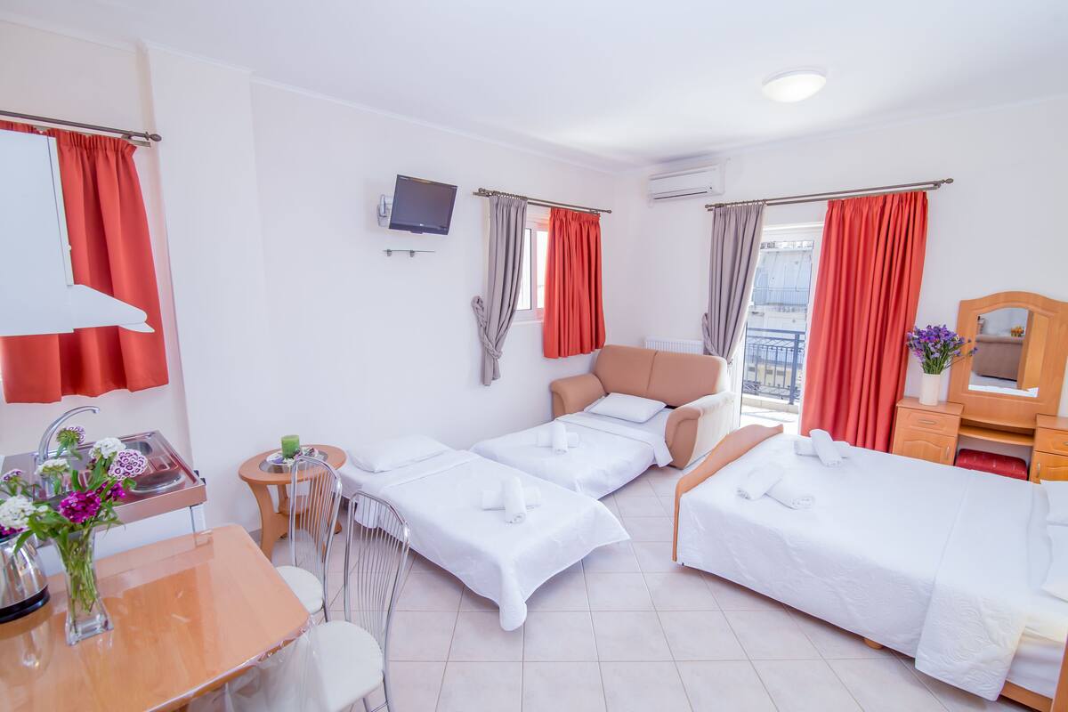 Ein Hotelzimmer mit zwei Einzelbetten, einem kleinen Tisch mit Stuhl, einem Fernseher und einem Fenster mit Vorhängen.
