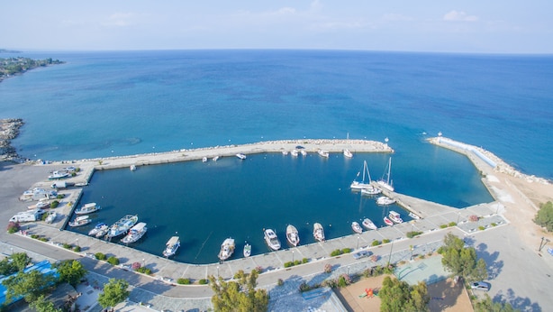 Vista aérea de un puerto deportivo con barcos amarrados, un muelle y un mar azul y despejado.