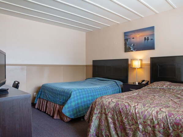 Habitación de hotel con dos camas, un escritorio, un televisor y un cuadro de una puesta de sol.